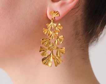 May include: Gold tone dangle earrings with a leaf design. The earrings are made of multiple layers of leaves that are connected together.