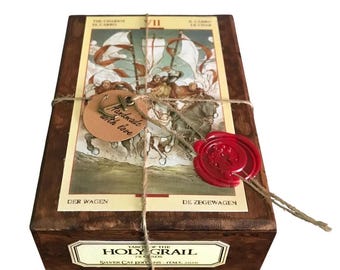 May include: A wooden box with a red wax seal and a tag that says "Handmade with love". The box contains a deck of tarot cards called "Tarot of the Holy Grail". The box is tied with twine.