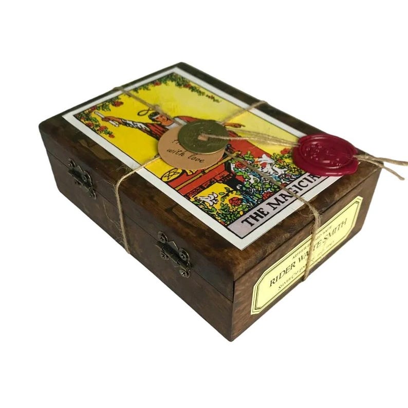 May include: A wooden box with a tarot card design on the lid, tied with twine and sealed with a red wax stamp. The box features metal clasps and a label that reads "Rider Waite Smith". The tarot card depicts "The Magician".