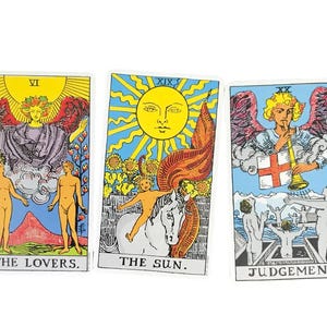 May include: Three tarot cards: "The Lovers," "The Sun," and "Judgement." Each card features vibrant illustrations with figures, symbols, and text. The cards have a white border and are set against a white background. The cards are colorful with yellow, blue, red, and orange.
