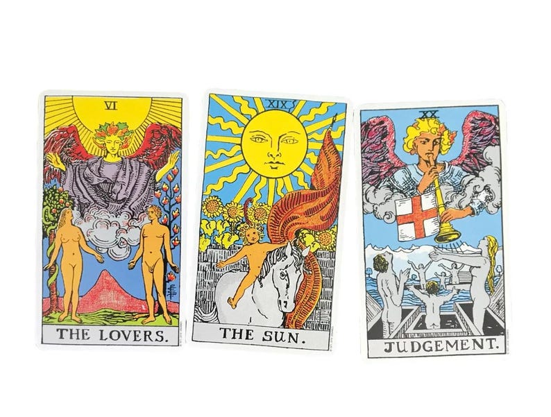 May include: Three tarot cards: "The Lovers," "The Sun," and "Judgement." Each card features vibrant illustrations with figures, symbols, and text. The cards have a white border and are set against a white background. The cards are colorful with yellow, blue, red, and orange.