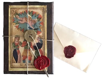 May include: A tarot card deck wrapped with twine, featuring a vintage illustration and a red wax seal. An ivory envelope with a matching seal is next to the deck. The card reads "L'AMORE".