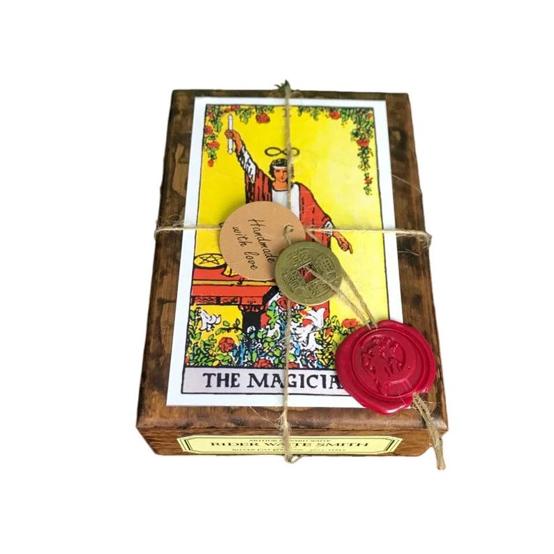 May include: A wooden box set of Rider-Waite Smith tarot cards, tied with twine. The box features a tarot card illustration of "The Magician" with a yellow background. Includes a red wax seal and a tag that says "Handmade with love."