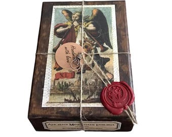 May include: A wooden box with a vintage illustration of an angel playing a trumpet. The box is wrapped in twine and has a red wax seal with a design. The box has a label that says "Handmade with love" and "Ancient Mine of Hate Etruria".