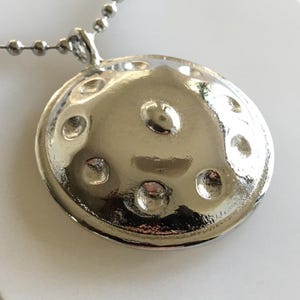May include: A silver handpan pendant necklace. The pendant is round and has eight indentations. The necklace is made of a silver chain.