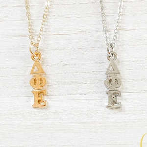 May include: Two silver necklaces with a pendant featuring the Greek letters Delta Phi Epsilon. The necklace on the left is gold and the necklace on the right is silver.