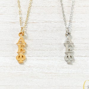 May include: Two necklaces with a pendant featuring the Greek letters AEPhi. The necklace on the left is gold and the necklace on the right is silver.