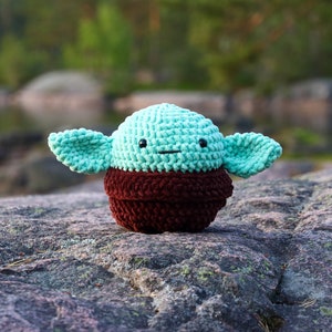 May include: A crocheted plush toy resembling a popular fictional character. The toy is green with brown accents and has a friendly expression.