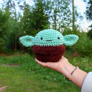May include: A crocheted green and brown plush toy resembling a popular fictional character. The toy has large ears and a small, round body.