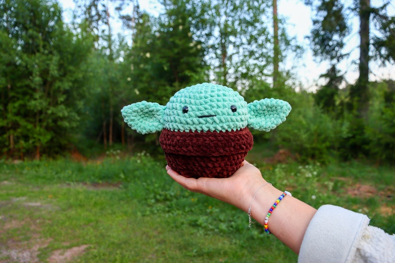 May include: A crocheted green and brown plush toy resembling a popular fictional character. The toy has large ears and a small, round body.