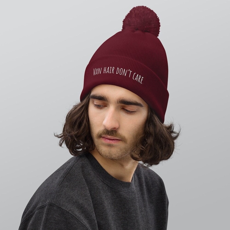 Peut inclure: Un bonnet bordeaux avec un pompon blanc sur le dessus. Le bonnet a le texte "VAN HAIR DON'T CARE" brod&eacute; &agrave; l'avant en blanc.