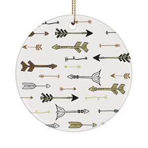 May include: A round white ceramic ornament with a gold string for hanging. The ornament features a pattern of black, brown, and gold arrows on a white background.