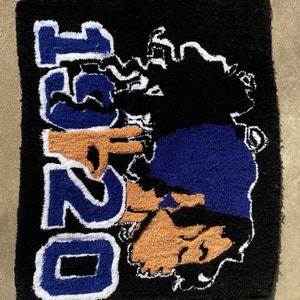 Puede incluir: Una alfombra negra con un dise&ntilde;o azul y blanco que dice "O251" y presenta una cara de dibujos animados con un sombrero azul y gafas de sol.