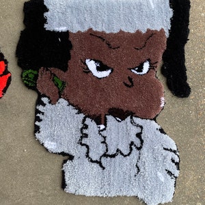 Puede incluir: Una alfombra con un personaje de dibujos animados con cabello negro, piel marr&oacute;n y una camisa blanca. El personaje tiene una expresi&oacute;n seria y est&aacute; sosteniendo un tel&eacute;fono verde en su o&iacute;do.
