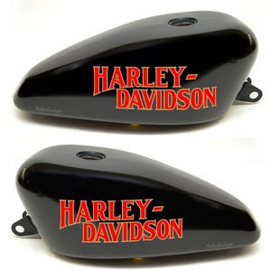 Op de afbeelding: Twee zwarte motorfiets benzinetanks met het Harley-Davidson logo in rode en gouden letters.