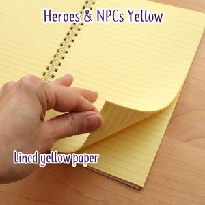 May include: A yellow spiral-bound notebook with lined paper. The text "Heroes & NPCs Yellow" and "Lined yellow paper" are visible. A hand is turning a page, revealing the yellow paper.