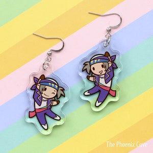 May include: A pair of clear acrylic dangle earrings featuring a cartoon character in purple and blue attire. The character has gray hair and a headband. The earrings have silver-colored ear wires and are set against a colorful striped background.