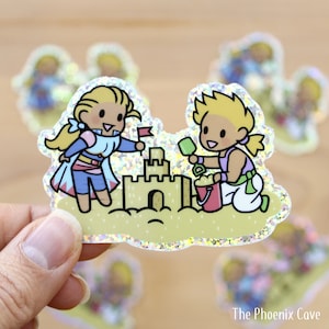 Könnte beinhalten: Ein glitzernder Aufkleber mit zwei Comicfiguren, die ein Sandburg am Strand bauen. Die weibliche Figur hat blonde Haare und trägt ein blaues und weißes Kleid. Die männliche Figur hat blonde Haare und trägt ein blaues und weißes Hemd und eine Hose. Die Sandburg ist aus gelbem Sand gebaut und hat eine rote Flagge oben drauf.