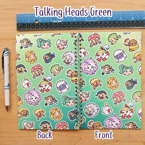 May include: A spiral-bound notebook with a green gradient background and a repeating pattern of cartoon faces. The notebook is labeled "Talking Heads Green" and has "Back" and "Front" labels. A ruler is placed above the notebook. A pen is on the left.