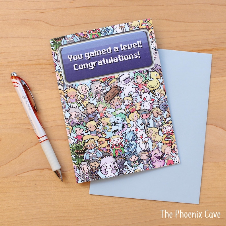 May include: Greeting card with a colorful cartoon design and the text "You gained a level! Congratulations!" A light blue envelope and a pen with red accents are next to the card. The Phoenix Cave logo is in the bottom right corner.