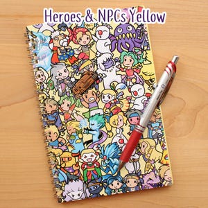 May include: A spiral-bound notebook with a yellow cover featuring cartoon characters and the text "Heroes & NPCs Yellow." A red and silver pen rests on the notebook. The notebook is on a wooden surface.