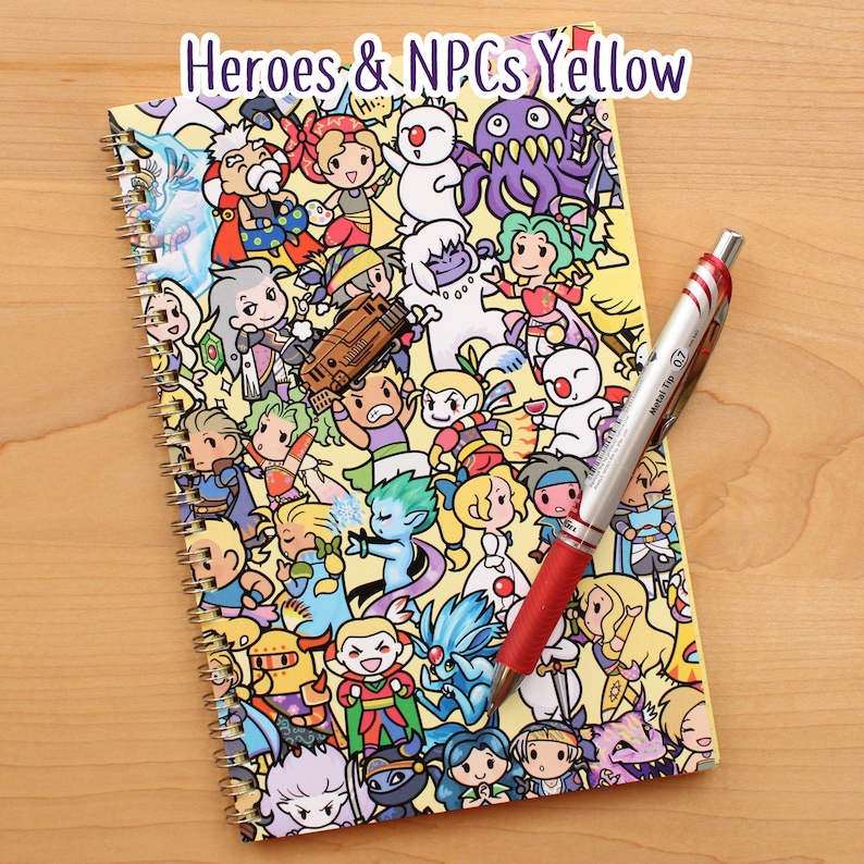 May include: A spiral-bound notebook with a yellow cover featuring cartoon characters and the text "Heroes & NPCs Yellow." A red and silver pen rests on the notebook. The notebook is on a wooden surface.