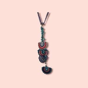 May include: A long, blue and white crocheted necklace with a turquoise and pink beaded tassel. The necklace features a series of crocheted circles with a layered design.