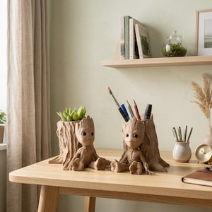 May include: Two Groot-themed desk organizers sit on a wooden table. One holds a succulent, the other pens and pencils. The organizers are brown and shaped like the character Groot from Guardians of the Galaxy. A notebook, clock, and vases are also on the table.
