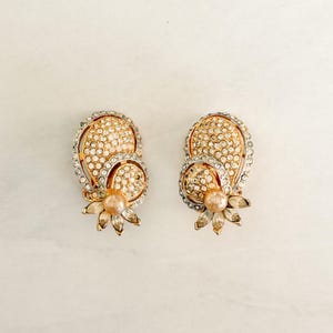 May include: A pair of vintage clip-on earrings. Each earring features a gold-toned, paisley-shaped design encrusted with clear rhinestones. A small, pearl-like bead sits at the center of a gold-toned floral accent.