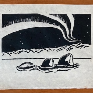 May include: Black and white linocut print of three whales swimming in the ocean under a starry sky with the aurora borealis in the background.