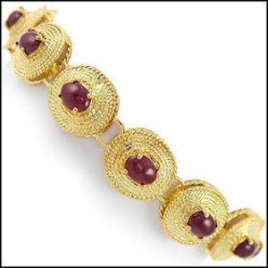 May include: Gold-toned bracelet featuring circular, textured links, each centered with a deep red gemstone. The bracelet's design showcases intricate detailing and a secure clasp, ideal for adding a touch of elegance to any outfit.