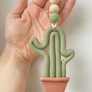 May include: A green clay cactus with a brown pot hanging from a string with wooden and green beads.