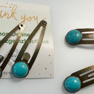 May include: Three antique gold hair clips with turquoise blue stones. Each clip has three prongs and a rounded stone.