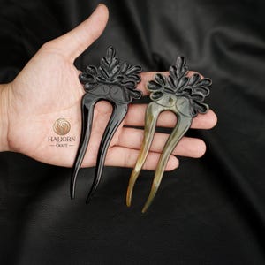 May include: Two hair combs made of horn with a decorative floral design. The comb on the left is black and the comb on the right is brown.