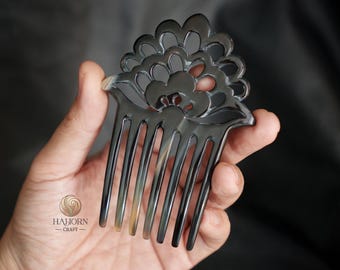 May include: A black horn comb with a floral design. The comb has seven teeth and a decorative top with a floral pattern.