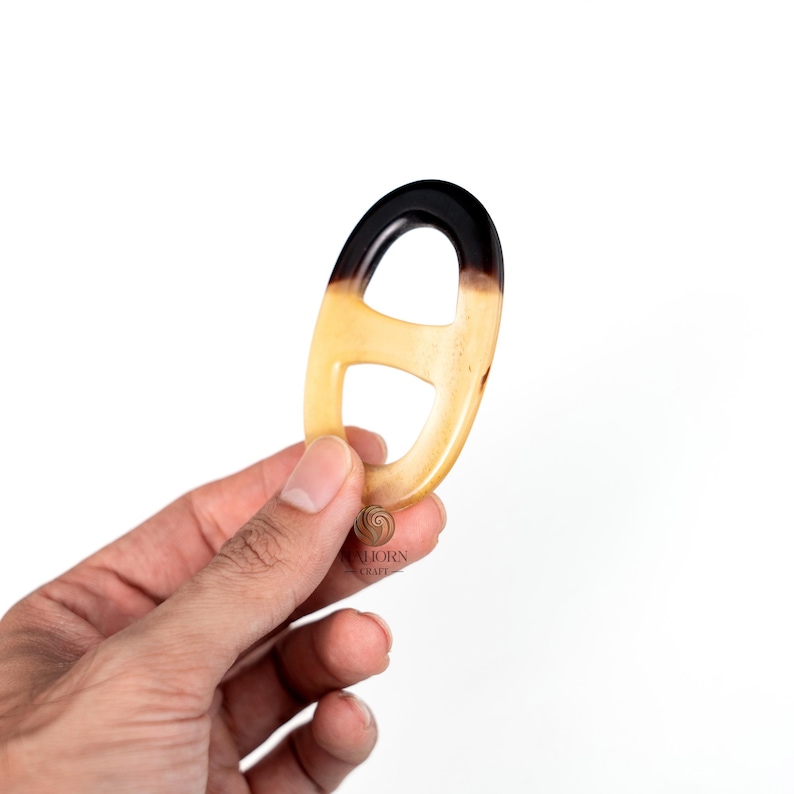 May include: A horn-shaped, oval-linked accessory with a gradient of colors. The top section is dark brown, transitioning to a light tan. The accessory is held against a white background.