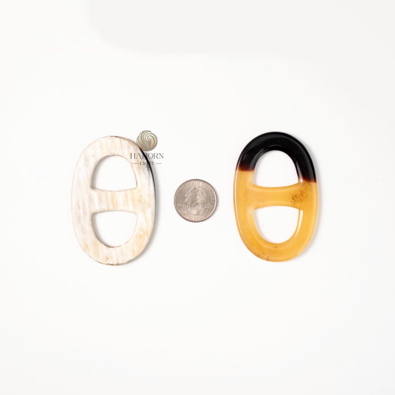 May include: Two oval-shaped decorative links, one off-white and the other amber with a black top, are displayed on a white surface. A US quarter coin is placed between them for size comparison. The links have a chain link design.