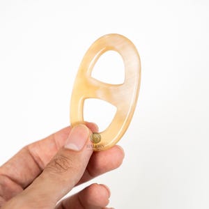 May include: A light tan, oval-shaped accessory with two openings, held in a hand. The object has a smooth, polished surface and a natural, marbled appearance. The logo "HALHORN - CRAFT" is visible.