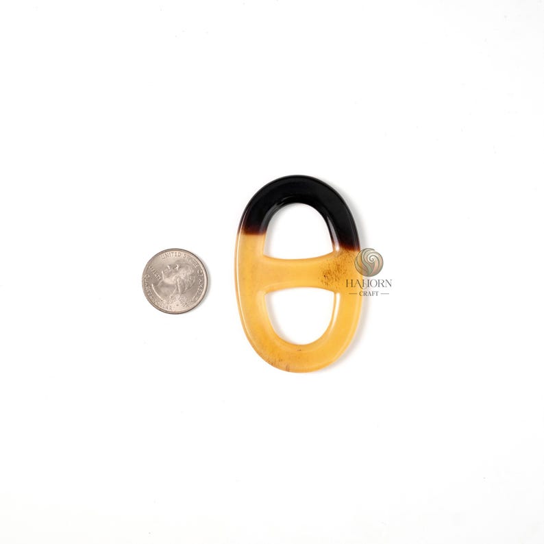 May include: A decorative, oval-shaped pendant with a gradient design. The top portion is black, transitioning to a light amber color. A US quarter is next to the pendant for size comparison. The pendant has a glossy finish.
