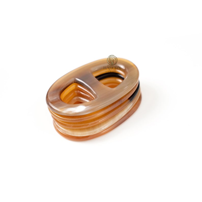 May include: A stack of oval-shaped, horn-like accessories in varying shades of brown and tan. Each piece has a central rectangular opening. The items are stacked on a white background.