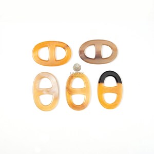 May include: Five oval-shaped decorative clasps in shades of tan, brown, and black. Each clasp features a central bar, creating a double-D shape. The clasps are arranged on a white surface. The brand name "HAJORN CRAFT" is visible.