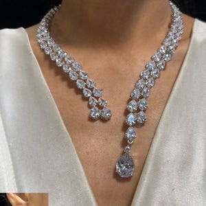 May include: A dazzling silver necklace and matching earrings set. The necklace features a double strand design with pear-shaped clear stones, culminating in a large teardrop pendant. The earrings mirror the necklace's design, creating a cohesive and elegant look.