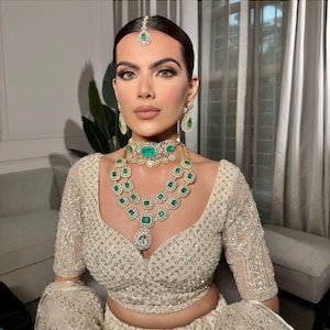May include: A woman wearing a white, beaded, and embroidered top with a layered emerald green and diamond necklace, matching earrings, and a small emerald green and diamond headpiece.