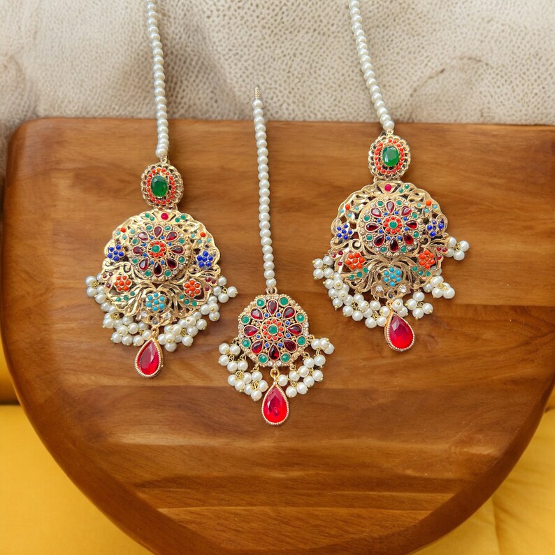 Op de afbeelding: Een set van drie gouden oorbellen met kleurrijke emaille en parel accenten. De oorbellen hebben een rond ontwerp met ingewikkelde details en een traanvormige hanger.