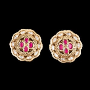 May include: A pair of gold-tone earrings with a circular design. The earrings are adorned with small white stones and pink gemstones.