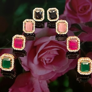 May include: A set of ten gold-tone earrings with various colored gemstones. The earrings feature a square-shaped setting with a clear crystal border. The gemstones are pink, red, green, and black.
