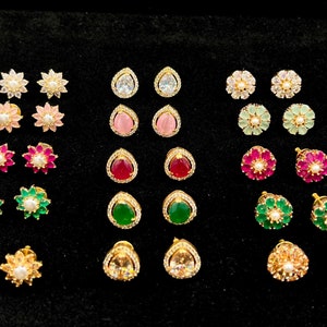 May include: A set of 20 gold stud earrings with various colored gemstones. The earrings feature a variety of shapes, including teardrop, round, and flower designs. The gemstones are set in gold and are surrounded by smaller diamonds.
