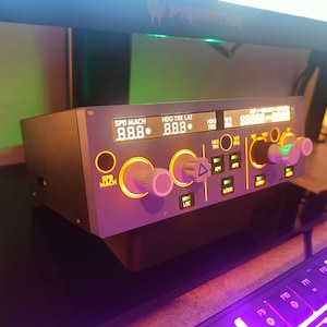 Könnte beinhalten: Ein graues und schwarzes Bedienfeld mit einem digitalen Display, das "SPD MACH 8.8.8." und "HDG TRK LAT 8.8.8." anzeigt. Das Bedienfeld verfügt über mehrere Knöpfe und Drehregler, darunter einen großen Drehregler mit der Bezeichnung "SPD MACH" und einen kleineren Drehregler mit der Bezeichnung "LOC".