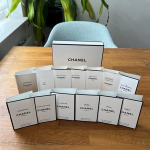 Può includere: Un assortimento di scatole di profumo Chanel, disposte su una superficie di legno. Le scatole bianche hanno bordi neri e il logo Chanel. I nomi delle fragranze includono "Gabrielle", "Coco" e "Gardenia".