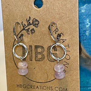 May include: A pair of silver hoop earrings with two stacked light pink gemstone beads hanging from each hoop. The earrings are displayed on a brown card with the text "HBGCREATIONS.COM".